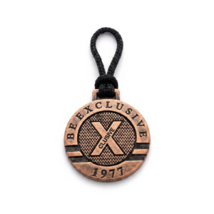 Chaveiro personalizado em metal com acabamento em tom de cobre, argola no topo e cordão de tecido preto acoplado.